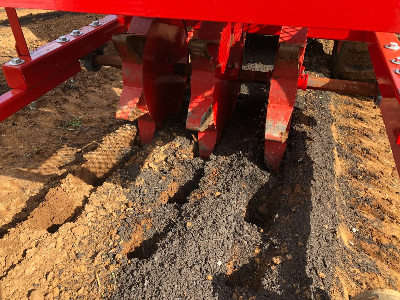 A PL-22 garlic planter working a field behind a tractor, with the planted row closing behind the machine.